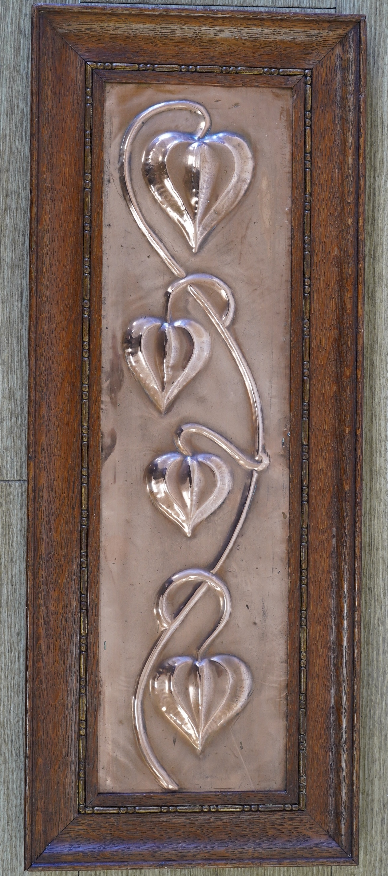 In the manner of Pearson, an Arts & Crafts embossed copper panel, oak framed, 59 x 24cm including frame. Condition - fair to good